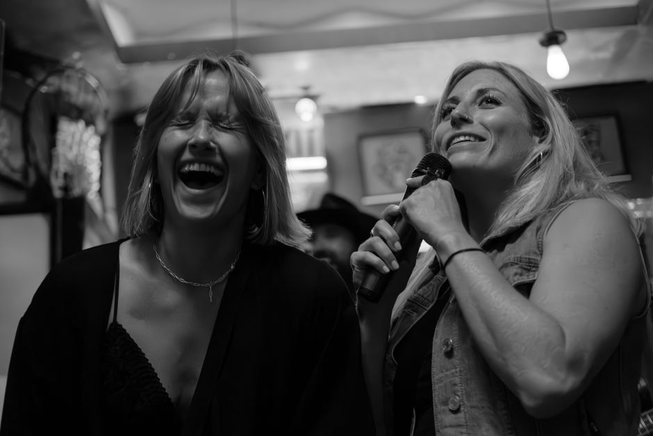 Two women laughing and singing at a karaoke night, exuding joy and camaraderie.